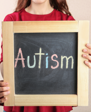 Child holding a chalkboard with the word autism, representing talking to kids openly about an autism diagnosis.
