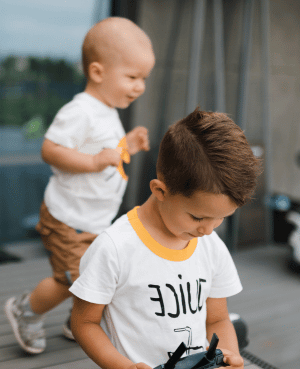 Older child holding a toy while baby sibling stands nearby, showing early sibling rivalry during play.