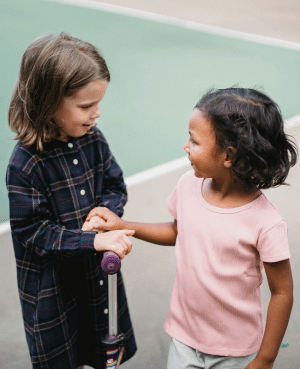 Two children talking outside, showing peer connection and support for language delays during playdates.