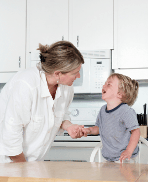Parent holding hands with a crying child in a kitchen, showing support during a difficult limit or transition.