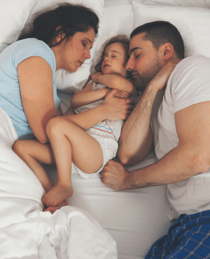 Parents co-sleeping with a child, showing nighttime connection and gentle sleep transitions.
