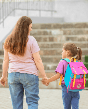 Caregiver walking with a child wearing a backpack, symbolizing support through anxiety and school transitions.