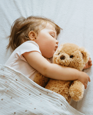 Sleeping toddler hugging a teddy bear, representing baby sleep, comfort, and responsive nighttime care.