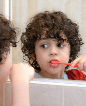 Young child brushing teeth in a mirror, illustrating calmer toddler tooth brushing without power struggles.