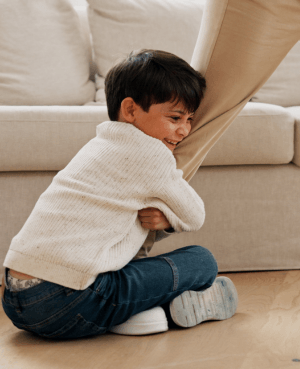 Young child holding onto a caregiver’s leg, representing clinginess, connection, and separation anxiety.