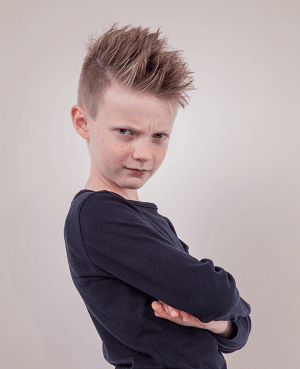 Boy standing with crossed arms, representing a strong-willed child resisting an everyday request.