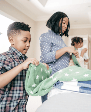 Mother and children folding laundry together, teaching household responsibility, teamwork, and independence.